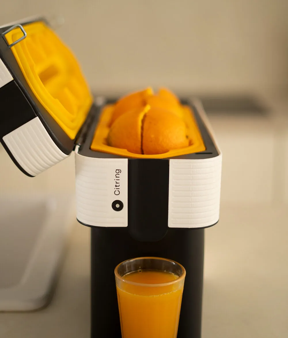 Citring One Orangenpresse mit geöffnetem Deckel und drei ganzen Orangen in der Presskammer